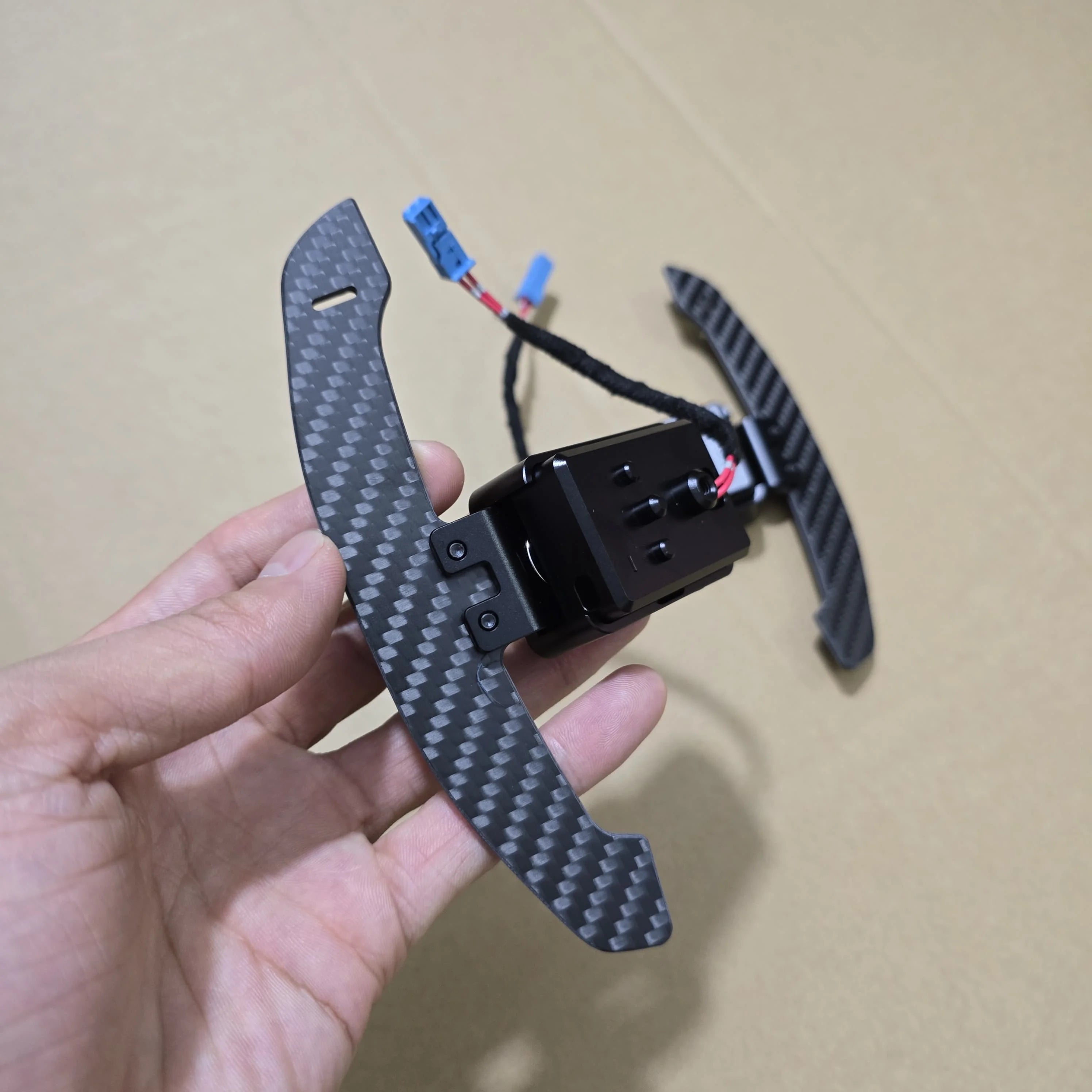 Carbon fiber wing with electronic components held by a hand on a beige background